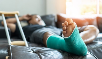 A man with his leg in a cast reclines on the living room couch