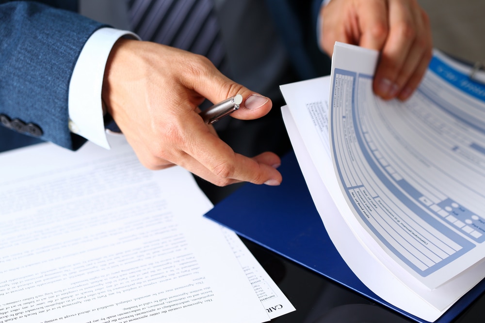 A close up of a man in a business suit's hands going through paperwork with a pen