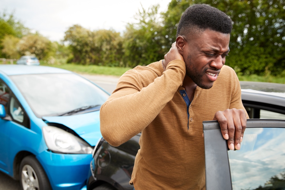 A man steps outside of his car and holds his neck in pain after getting in an accident