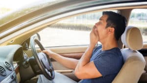 Young man driving a car and feeling sleepy.