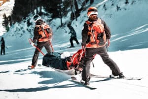 Rescuers at a ski resort evacuate the victim from the slope. Two lifeguards descend a tourist on a special sled on a sunny winter day. Blurred background, toned