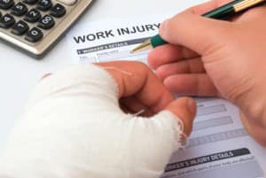 A man filling up a work injury claim form with a wrapped hand