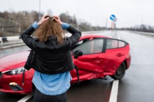 A woman looking at her car with her back to the camera after a hit-and-run accident