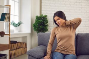 Young woman sitting at home, holding her neck in pain from a previous car accident.