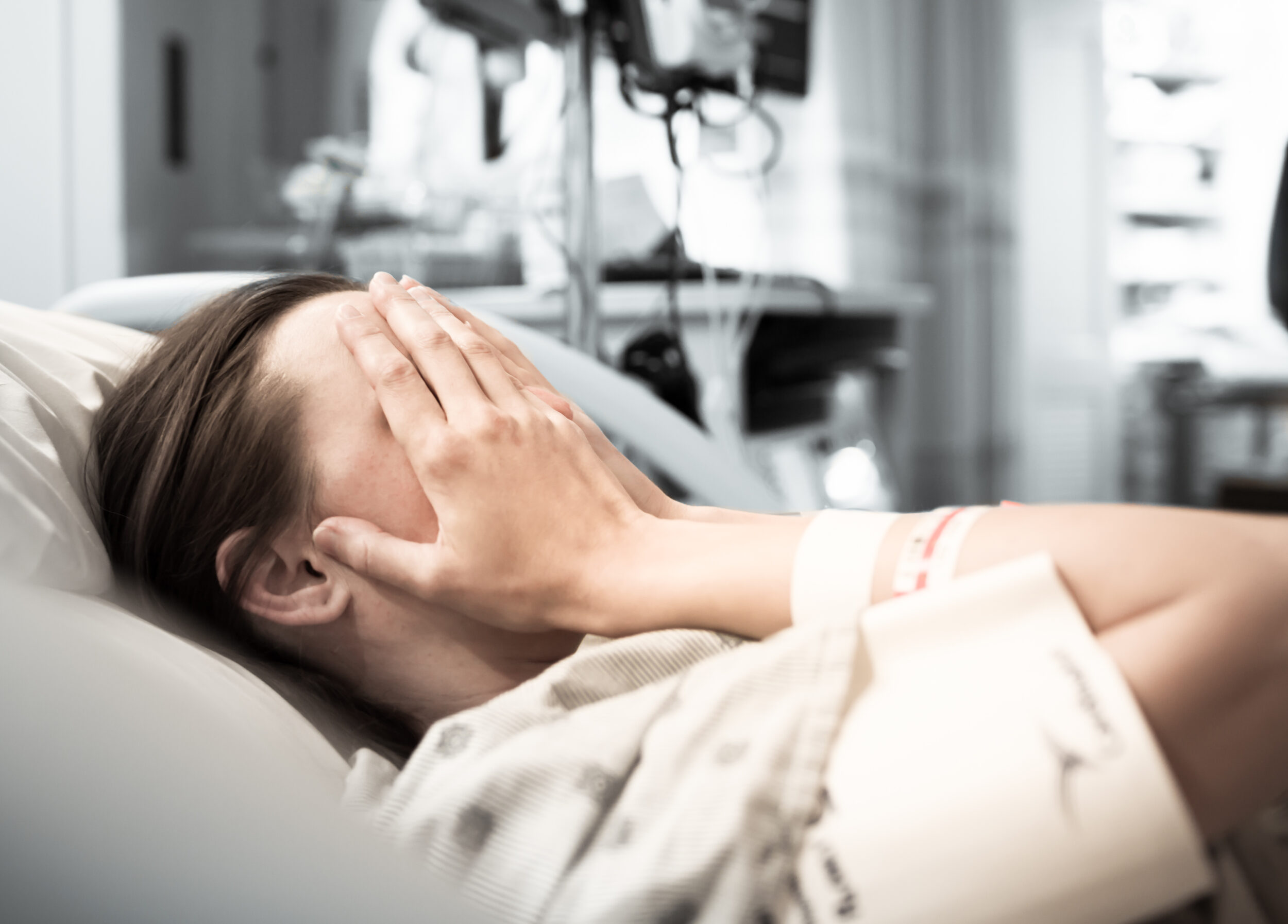 woman in hospital bed, covering her face with her hands in pain.