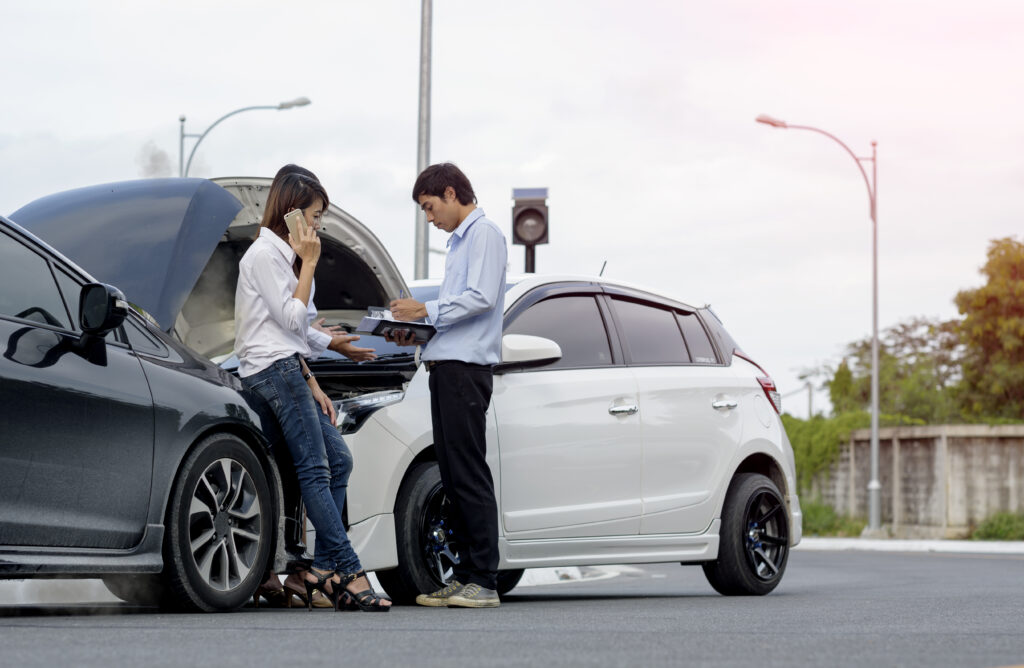 Two people standing in front of a car accident and making calls to their insurance and injury attorneys.