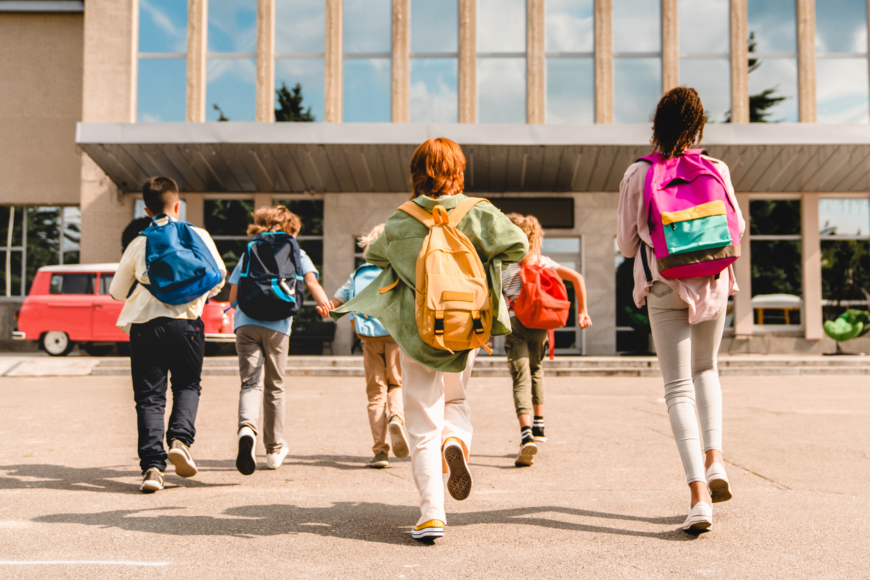 Policeman going over car accident scene Students with backpacks running toward a school building for a school-sponsored activity.